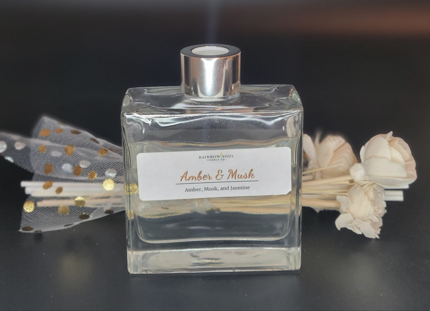 Clear diffuser bottle with silver cap and decorative flowers on a dark background