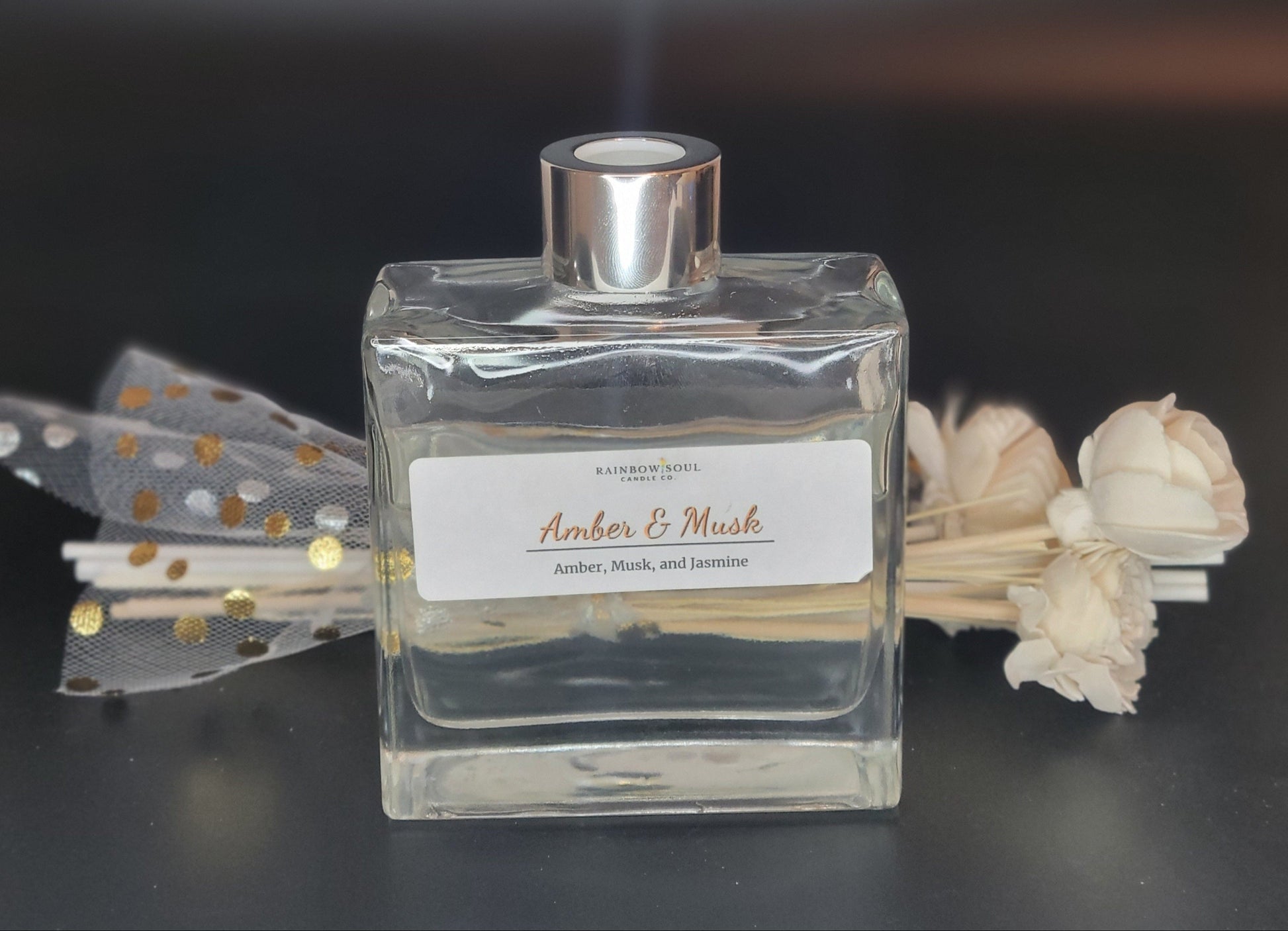 Clear diffuser bottle with silver cap and decorative flowers on a dark background